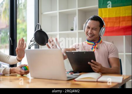Ein attraktiver und fröhlicher asiatischer Homosexueller spricht gerne mit ihm, während er mit seinem Gast in seinem Sendestudio einen Audio-Podcast aufnimmt. Stockfoto