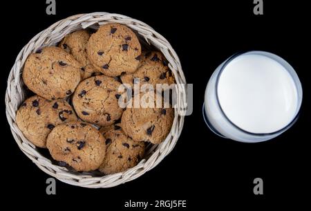 Frische Milch und Schokoladenkekse in einem Bambuskorb, isoliert auf schwarzem Hintergrund Stockfoto