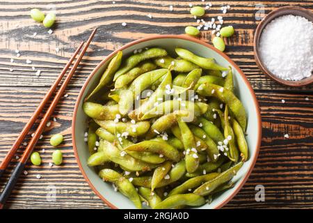 Gebratene grüne Edamame-Sojabohnen mit Meersalz und Sesamsamen auf dem Teller auf dem Tisch. Horizontale Draufsicht von oben Stockfoto
