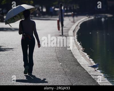 Ein Dateifoto vom 10.08/2022, auf dem ein Geher unter einem Regenschirm im Schatten steht, während er bei heißem Wetter neben der Serpentine im Hyde Park, London, spaziert. Das Vereinigte Königreich braucht eine "kulturelle Veränderung" in der Art und Weise, wie Menschen über Hitzewellen denken, sagte das britische Rote Kreuz, nachdem Umfragen ergeben hatten, dass mehr als ein Drittel der Erwachsenen dies nur als ein zukünftiges Problem sehen. In einer europaweiten wissenschaftlichen Studie wurde kürzlich geschätzt, dass im vergangenen Sommer im Vereinigten Königreich mehr als 3.000 Menschen an Hitze starben, während das Amt für nationale Statistik in diesem Zeitraum etwa die gleiche Anzahl von Todesfällen verzeichnete. Ausgabedatum: Donnerstag, 10. August 20 Stockfoto