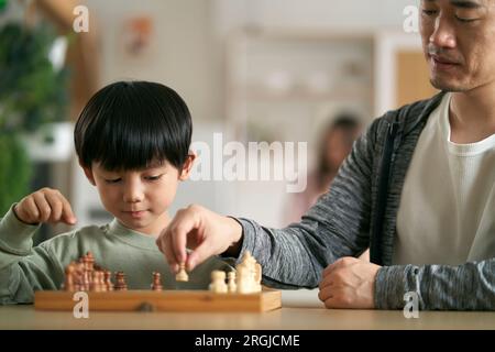 asiatischer Vater und Sohn sitzen zu Hause am Küchentisch und spielen Schach Stockfoto