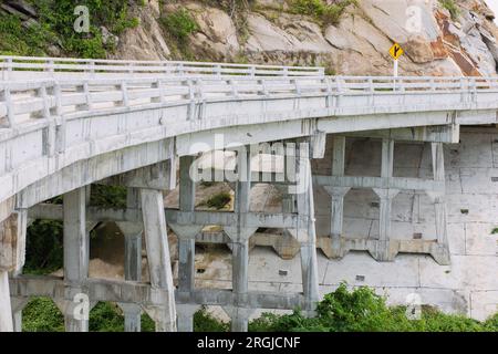 Starre Balken und Säulen unter der Brücke Eine Balkenstruktur mit festen Säulen einer parallelen Betonbrücke zum Überqueren des Flusses in der Untersicht. Stockfoto