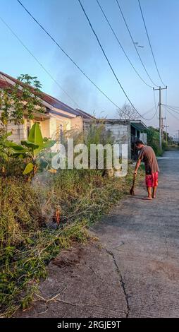 Bogor, Indonesien - 01. August 2023: Ein Mann räumte das Gras am Straßenrand und zündete es an Stockfoto