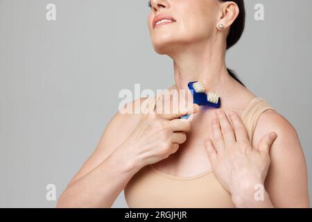 Reife Frau mit Gesichtswalze für glatten Nackenbereich auf grauem Studiohintergrund. Zugeschnittenes Bild. Stockfoto