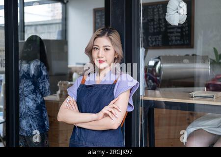 Glückliche junge Kellnerin, die am Eingang des Restaurant-Coffee-Shop steht, um Kunden, kleine Unternehmen, junger asiatischer Besitzer, Einzelhandel, CO, willkommen zu heißen Stockfoto