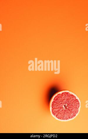 Nahaufnahme der Hälfte der roten Grapefruit und des Kopierbereichs auf orangefarbenem Hintergrund Stockfoto