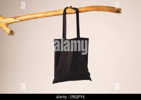 Schwarze Segeltasche, die am Holzzweig hängt, mit Kopierbereich auf weißem Hintergrund Stockfoto