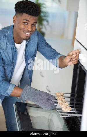 Ein hübscher Mann, der ein Tablett mit gebackenen Keksen herausnimmt Stockfoto