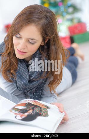 Junge Frau, die eine Zeitschrift liest, die auf dem Boden liegt Stockfoto