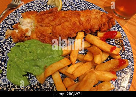 Traditioneller britischer Fisch und Chips, mit matschigen Erbsen. Es wird drinnen in einem Pub mit einem Pint Bitter serviert Stockfoto