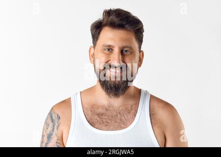 Porträt eines gutaussehenden, lächelnden, bärtigen Mannes im Singlet, der vor weißem Studiohintergrund in die Kamera schaut Stockfoto
