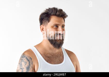 Attraktiver, reifer, lächelnder, bärtiger Mann im Singlet, der vor weißem Studiohintergrund wegschaut Stockfoto