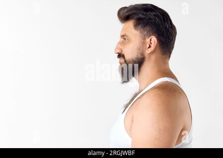 Seitenansicht eines gutaussehenden, reifen, lächelnden, bärtigen Mannes im Singlet, der direkt vor dem weißen Studiohintergrund schaut Stockfoto