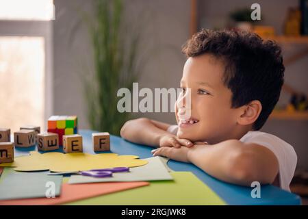 Foto eines positiven, traumhaften süßen Jungen mit Beistelltisch über die Annahme von Familienbetreuung in einem gemütlichen Zimmer im Haus Stockfoto