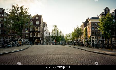 Brücke über den Kanal in Amsterdam am Samstagnachmittag. Zahlreiche Fahrräder parken in der Nähe des Geländers und einige Fußgänger laufen im Hintergrund Stockfoto