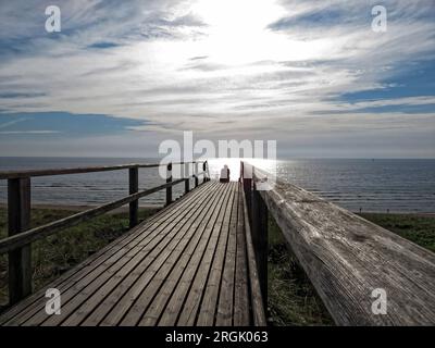 Der Mensch sitzt auf einem hölzernen Pfad und schaut auf das Meer Stockfoto