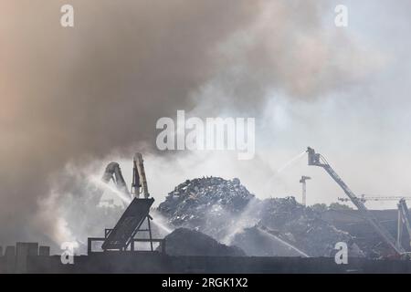 Duisburg, Deutschland. 10. Aug. 2023. Die Feuerwehr löscht weiterhin den Großbrand im Hafen von Duisburg, der seit Stunden auf der Schrottinsel ausbricht. Im Hafen auf der Schrottinsel brach am Donnerstag, 09.08.2023 Uhr, ein Feuer auf einem Recyclingplatz mit Altfahrzeugen aus. Etwa 100 Tonnen Schrott brannten, sagte ein Sprecher der Feuerwehr. Kredit: Christoph Reichwein/dpa/Alamy Live News Stockfoto