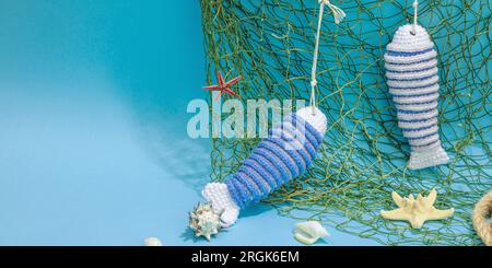 Handgefertigtes Marinekonzept. Gestrickte Sardinenfische im nautischen Stil. Fischernetz, traditionelle Einrichtung im Meer. Hartes Licht, dunkler Schatten, trendy blauer Hintergrund Stockfoto