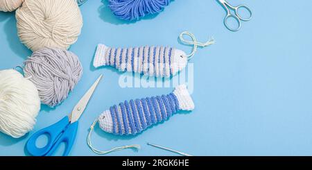 Handgefertigtes Marinekonzept. Gestrickte Sardinenfische, Einrichtung im nautischen Stil, traditionelles Meeresdekor. Hartes Licht, dunkler Schatten, trendy blauer Hintergrund, Bannerform Stockfoto