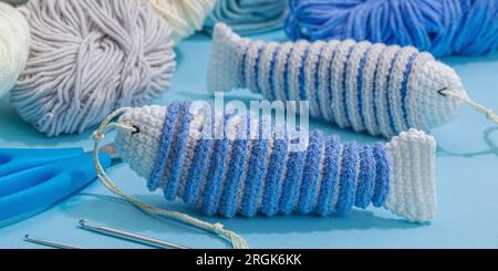 Handgefertigtes Marinekonzept. Gestrickte Sardinenfische, Einrichtung im nautischen Stil, traditionelles Meeresdekor. Hartes Licht, dunkler Schatten, trendy blauer Hintergrund, Bannerform Stockfoto