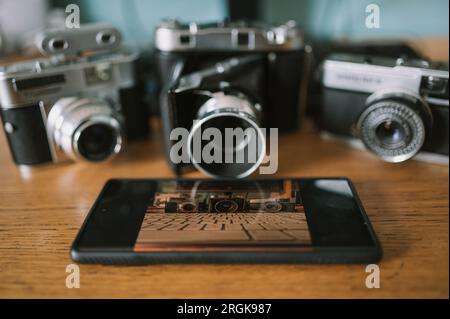 Drei klassische Kameras neben einem modernen Kameratelefon, die das Alte und das Neue illustrieren. Stockfoto