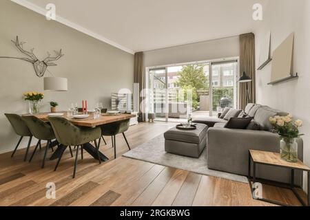 Ein Wohnzimmer mit Holzfußboden und grauen Sofas vor dem Sofa ist ein kleiner Esstisch Stockfoto