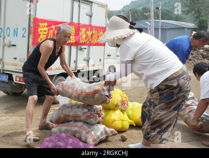 Baoding, Chinas Provinz Hebei. 10. Aug. 2023. Dorfbewohner bringen gespendetes Gemüse in Ligezhuang Village in Zhaogezhuang Town, Laishui County, Nordchina Provinz Hebei, 10. August 2023. Einige Dörfer im Bezirk Laishui waren von Starkregen betroffen und stießen auf Verkehrs- und Kommunikationsstörungen. Die lokalen Behörden haben sich nach Kräften bemüht, die durch Überschwemmungen beschädigte Infrastruktur zu reparieren und gleichzeitig von der Regierung gekaufte Hilfsgüter zu liefern, die von allen Lebensbereichen an die von Überschwemmungen betroffenen Einwohner gespendet werden. Kredit: Yang Shiyao/Xinhua/Alamy Live News Stockfoto