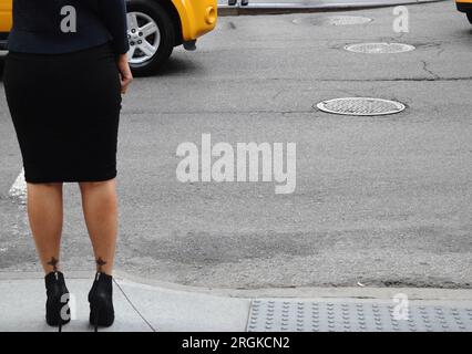 Eine Frau mit schwarzem Bleistiftrock und hohen Absätzen wartet darauf, die Straße zu überqueren Stockfoto