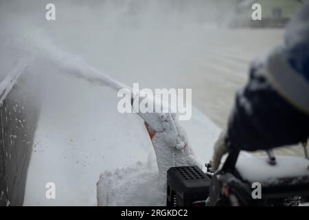 Schneefluss aus der Steckdose der Schneeräumausrüstung. Schneeräumung im Stadion. Herstellung einer Eislaufbahn für das Schlittschuhlaufen. Eisreinigung. Stockfoto