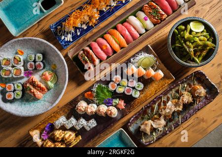 Genießen Sie köstliches Sushi und Brötchen mit frischem Fisch und grünen Erbsen auf einem Holztisch in einem hellen Café Stockfoto