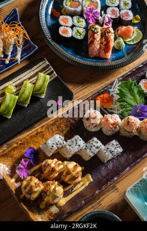 Von oben gibt es leckere frische Sushi-Brötchen mit verschiedenen Belägen, serviert auf Tabletts mit dekorativen Blumen auf einem Holztisch im Café Stockfoto