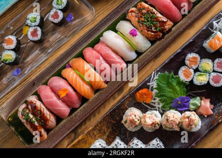 Blick von oben auf die Fülle an traditionellem japanischem Sushi und Brötchen mit frischem Fisch, serviert auf Tabletts in einem leichten Café Stockfoto