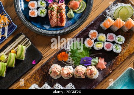 Von oben gibt es verschiedene leckere Sushi-Brötchen mit Fisch, serviert auf Tabletts mit Scheiben Limette und dekorativen frischen Blumen Stockfoto