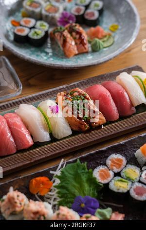 Von oben gibt es eine Fülle an köstlichem Sushi und Brötchen mit verschiedenen bunten Fischen, serviert auf Teller und Tabletts in einem leichten Café Stockfoto