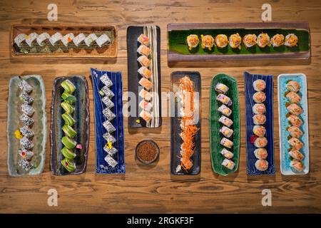 Blick von oben auf verschiedene Sushi-Brötchen mit Fisch und Sojasauce auf verschiedenen Marmorplatten auf Holzhintergrund im Restaurant Stockfoto