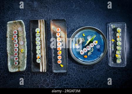 Blick von oben auf verschiedene Maki-Brötchen, serviert auf verschiedenen Marmorplatten auf einem blauen Marmortisch Stockfoto