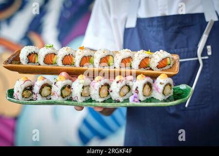 Ein anonymer Chefkoch mit köstlichen Sushi-Brötchen mit verschiedenen Geschmacksrichtungen, serviert auf Marmortabletts im Restaurant vor verschwommenem Hintergrund Stockfoto