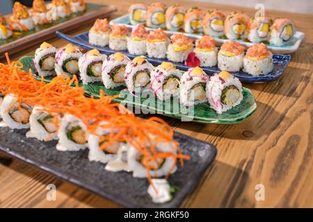 Von oben aus werden verschiedene appetitliche Uroamaki Sushi-Brötchen auf Marmortabletts auf einem Holztisch serviert Stockfoto