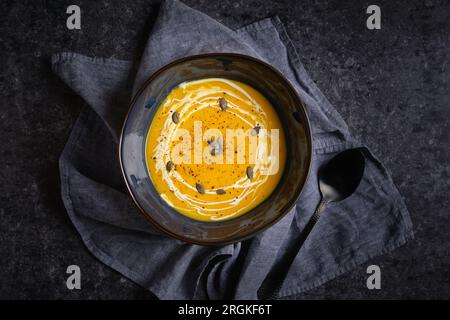 Von oben: Köstliche Herbstcremesuppe aus Kürbissen, serviert auf Serviette mit Löffel auf schwarzem Hintergrund Stockfoto