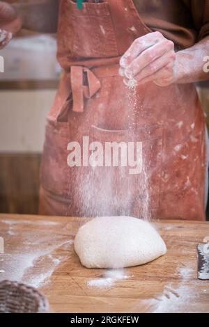Männliche Bäckerhände arbeiten Brotteig mit Mehl auf einem Holztisch. Stockfoto