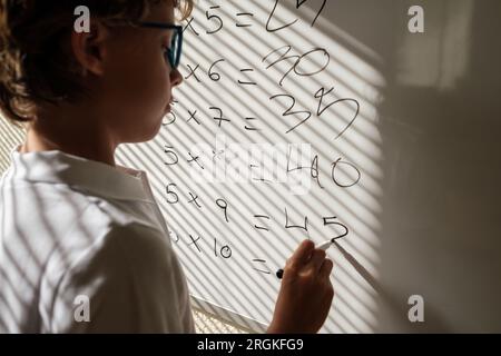 Seitenansicht des fokussierten intelligenten Schulkindes in einer Brille, die mathematische Beispiele während des Unterrichts an der Schule auf dem Whiteboard löst Stockfoto
