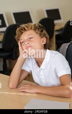 Gelangweiltes und müdes Schulkind, das sich während des Unterrichts in der Schule an einem Tisch im Klassenzimmer lehnte Stockfoto