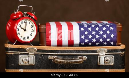 Oldtimer-Koffer mit Wecker und Flagge. Banner „Reise“, „Reise“, „Urlaub“ oder „Umzug in die USA“. Stockfoto