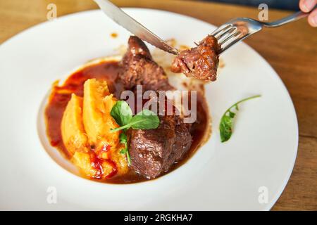 Detail der Gabeln, in denen eine Person ein Stück Fleisch aus einer Schale Kalbbacken mit Kokosnuss-Mojo und Thunfischpüree mit Orangensauce s hält Stockfoto