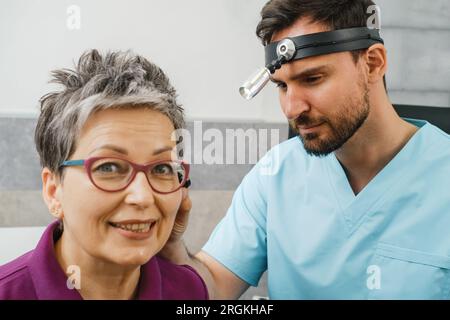 Oto-Laryngologe bei der Untersuchung von Frauen mittleren Alters im modernen medizinischen Zentrum. Porträt eines Audiologen zur Beurteilung von Hörstörungen. Ohrmodell am Stockfoto