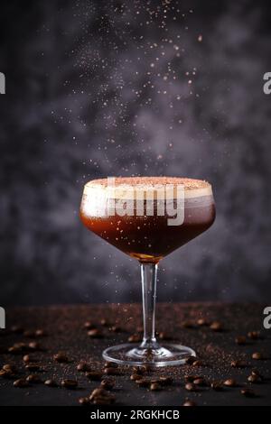 Köstlicher Cocktail, dekoriert mit geriebener Schokolade in Kampagnen-Coupé-Glas, auf einem schwarzen Tisch unter verstreuten aromatischen Kaffeekörnern in der Bar platziert Stockfoto