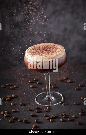 Coupé-Glas von oben mit frisch zubereitetem Cocktail, dekoriert mit geriebener Schokolade, auf einer schwarzen Theke zwischen aromatischen Kaffeekörnern in der Bar platziert Stockfoto