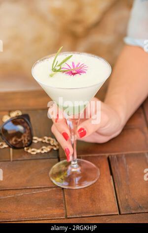 Aus einem hohen Winkel, eine Frau, die sich nicht wiedererkennt, nimmt ein Glas erfrischenden Cocktail mit Dekoration auf einem Holztisch Stockfoto