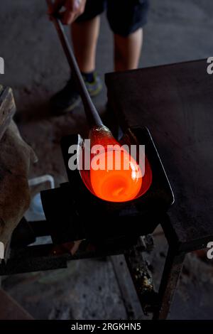 Unbekanntes männliches Glasbläser im Prozess der Herstellung einer Wasservase mit heißem Flüssigglas auf Metallmarder mit Pontil während der Arbeit Stockfoto