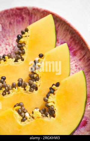 Nahaufnahme exotischer Papaya-Früchte mit in Stücke geschnittenen Samen, serviert auf rosafarbener Keramikplatte auf verschwommenem Hintergrund Stockfoto
